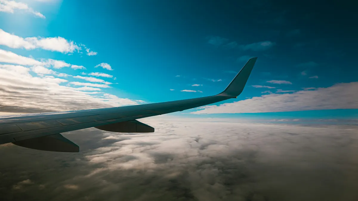 Tragfläche eines Passagierflugzeugs über einer Wolkendecke bei blauem Himmel