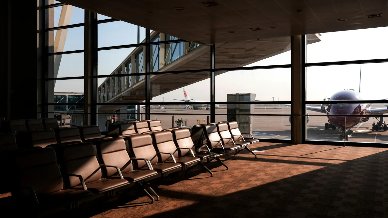 Leerer Wartebereich am Flughafen mit Sitzreihen, durch die Fenster ist ein Flugzeug am Gate zu sehen